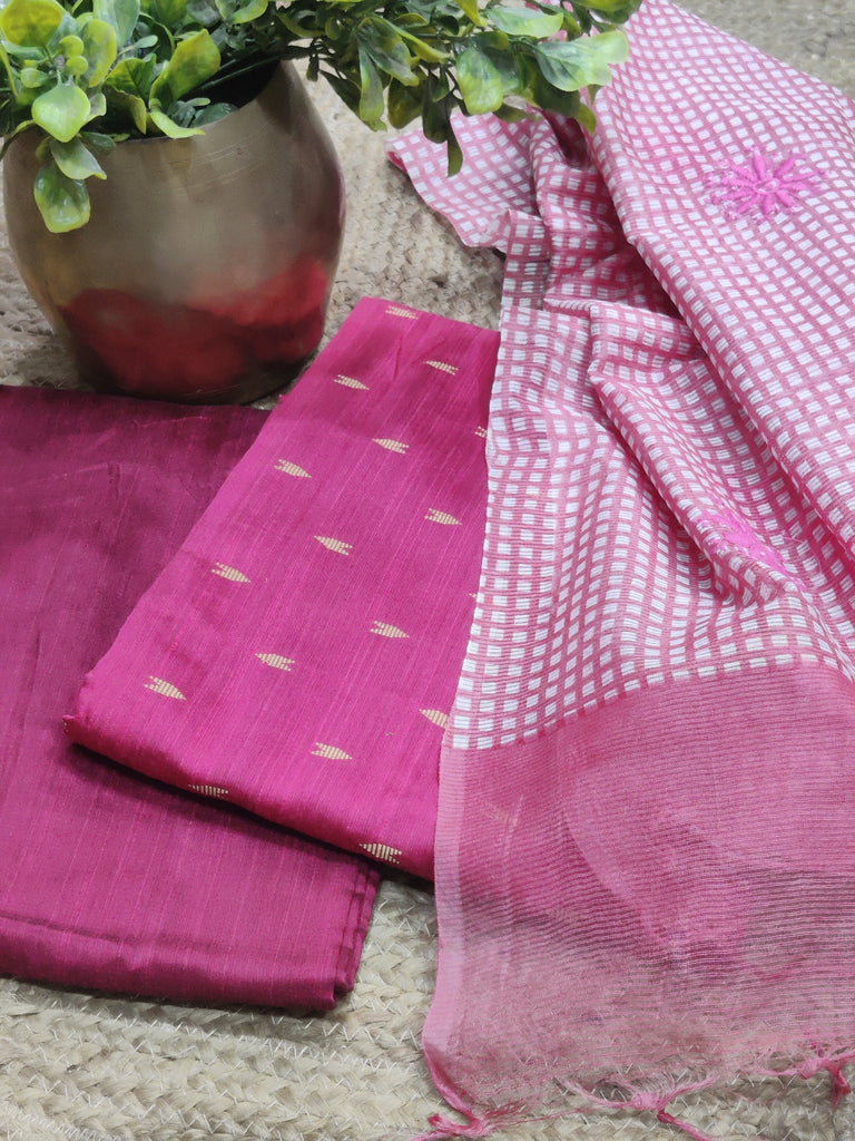 Pink fabric with white patterns on a textured surface with a plant in the background