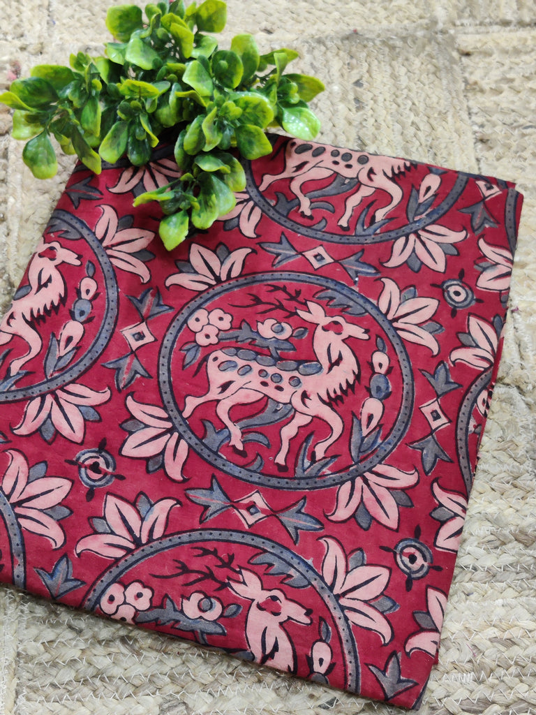 Red fabric with deer pattern on a stone surface with green leaves.