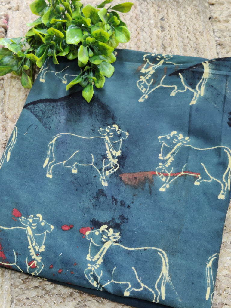 Fabric with cow pattern on a blue background, held by green leaves.