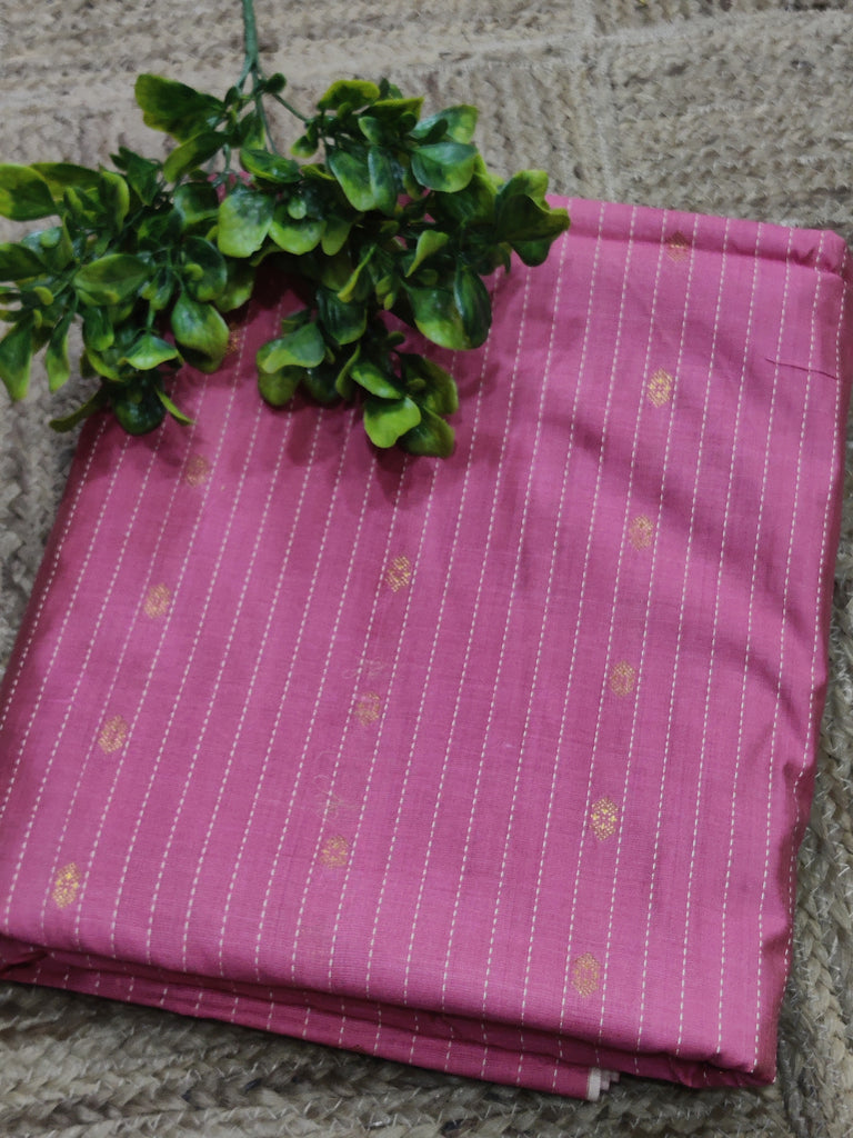 Pink fabric with gold patterns on a stone surface with green leaves.