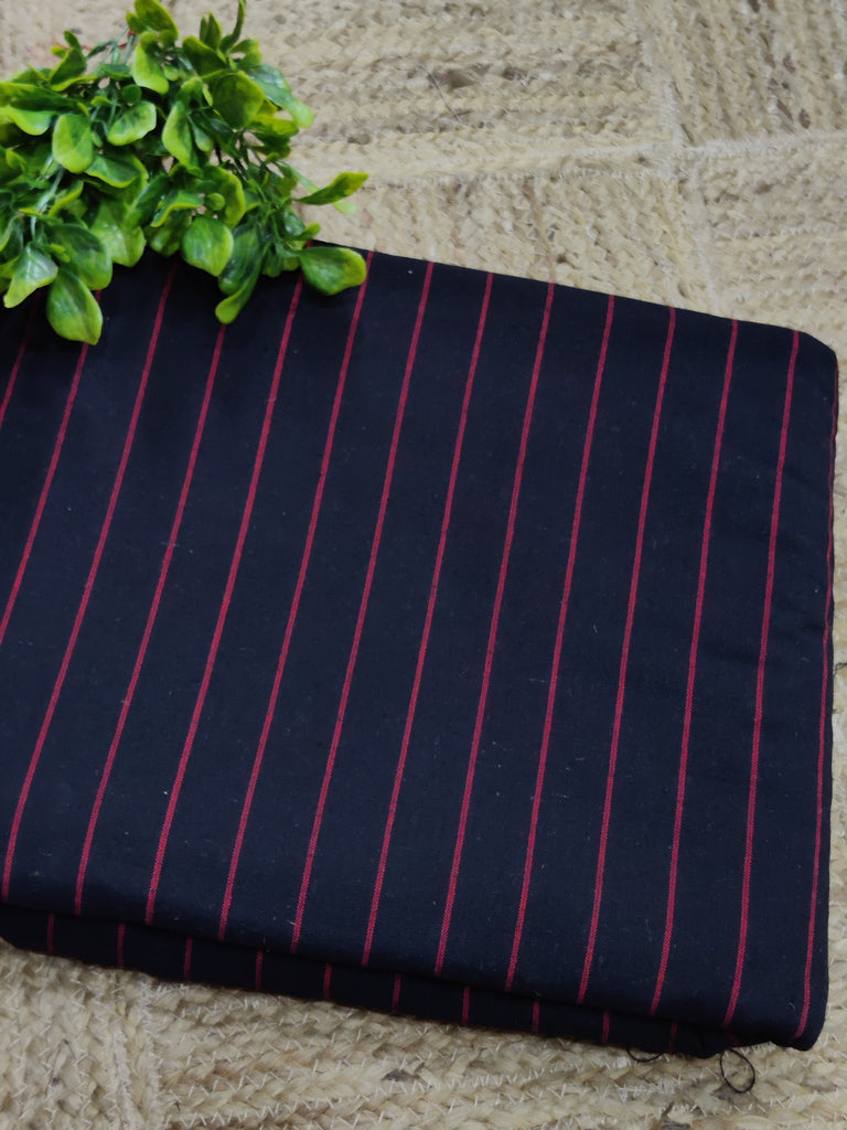 Black fabric with red stripes on a stone surface with green leaves.