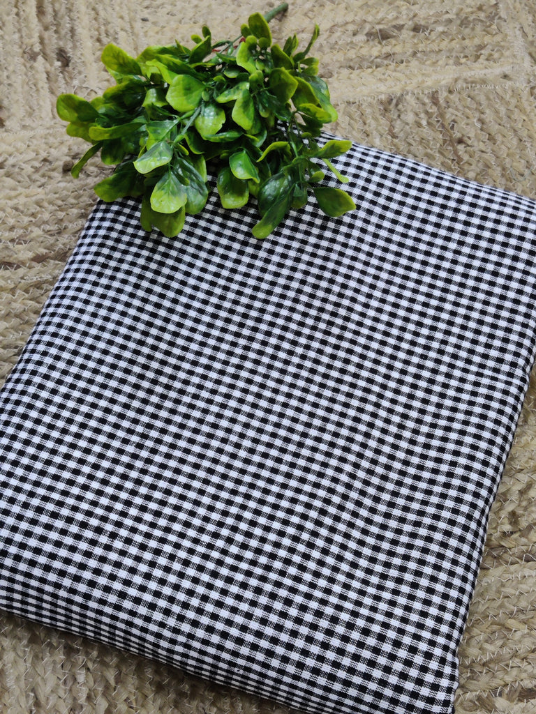 Black and white checkered fabric with a green plant on a stone surface