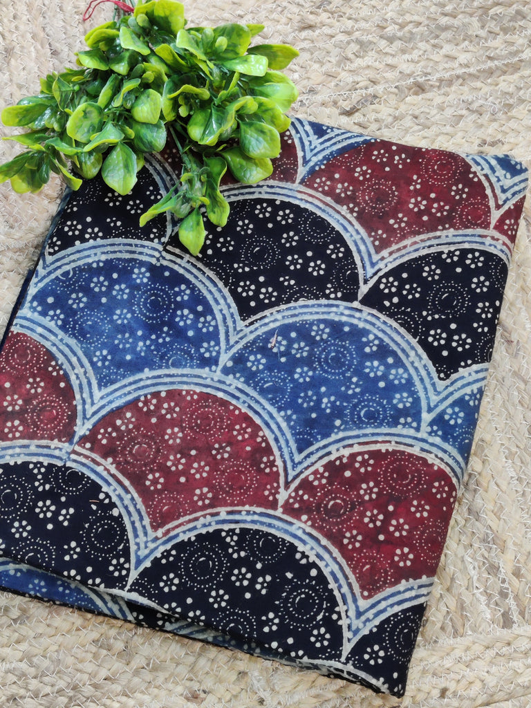 Fabric with a blue and red pattern on a stone surface with a plant.