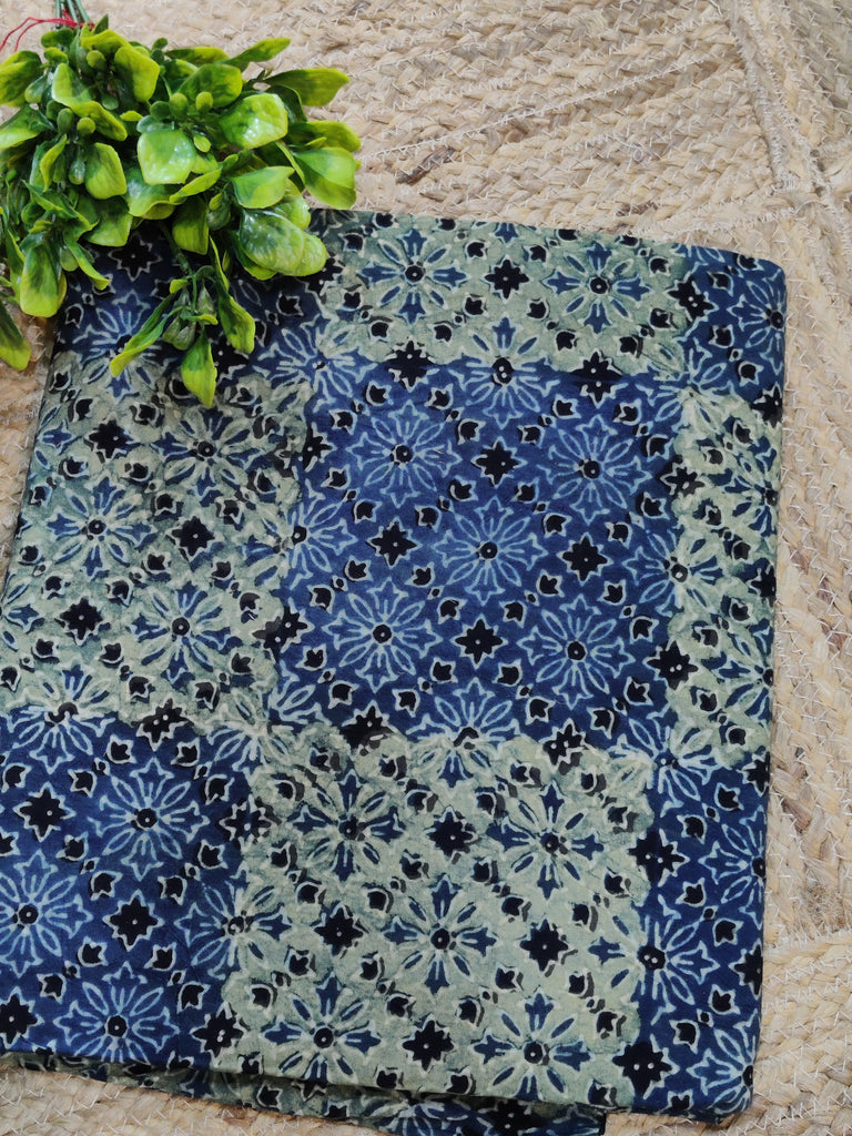 Two patterned fabric squares on a stone surface with green leaves.
